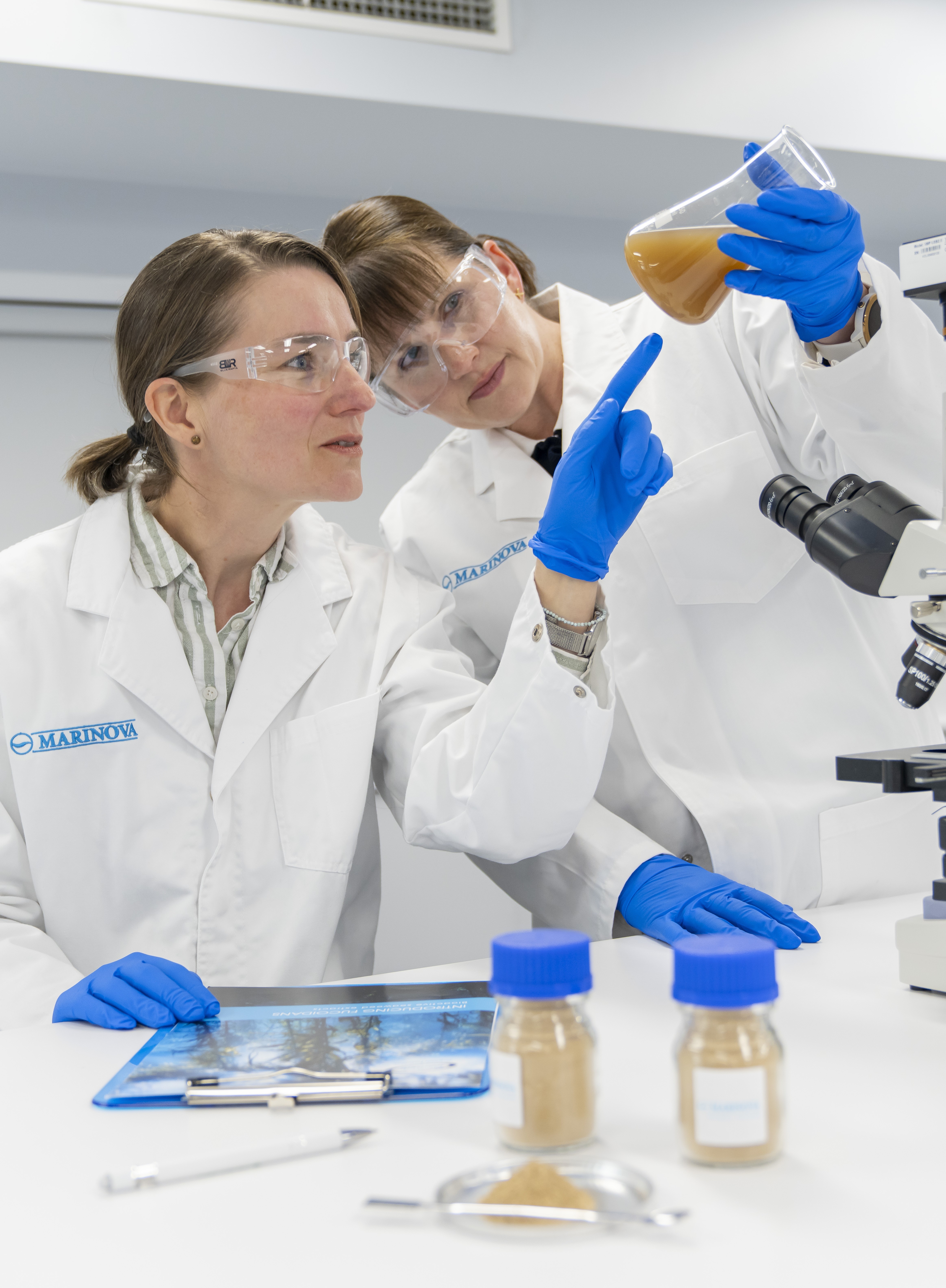 Two Marinova researchers in the lab, examining a brown liquid in a flask