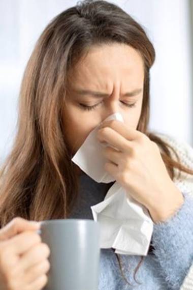 Woman sitting on couch blowing her nose