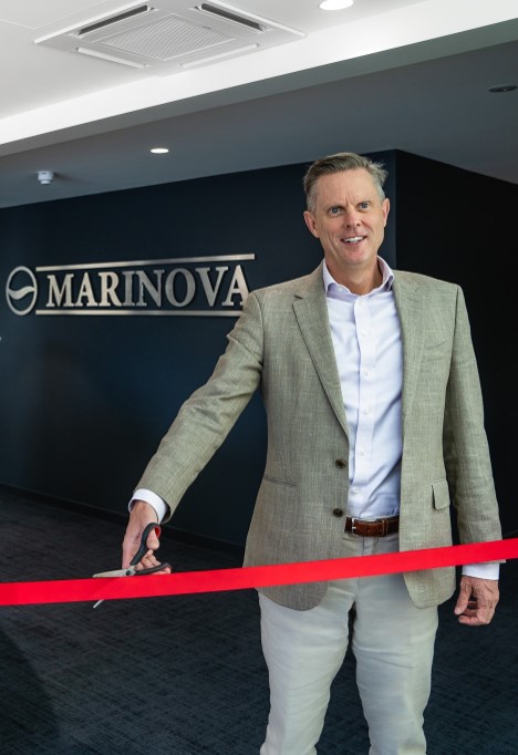 CEO Paul Garrott standing in front of a Marinova sign and cutting a red ribbon whilst smiling. 